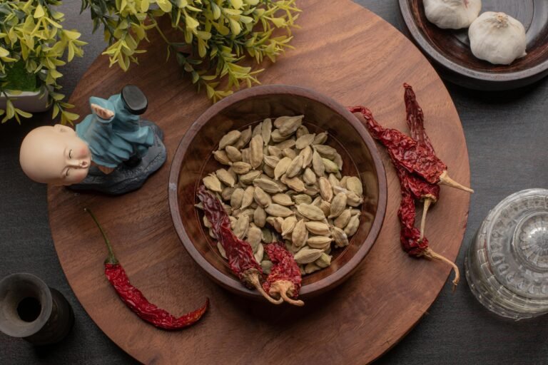 Flat lay of cardamom and dried chilies in bowls on a wooden surface with decorative elements.